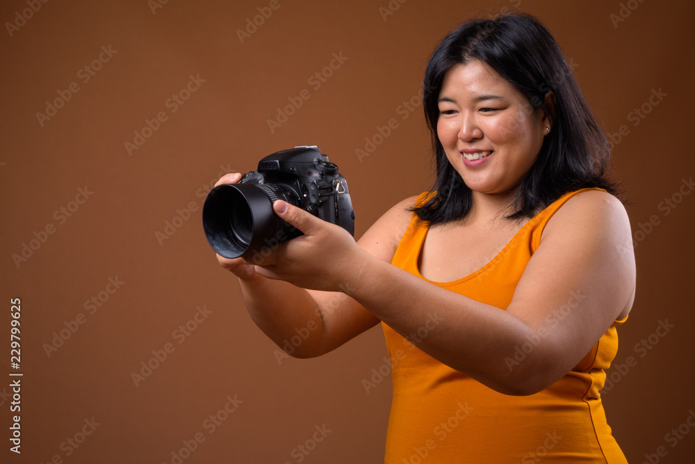 Fototapeta premium Beautiful overweight Asian woman photographer using camera