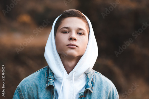 Teen boy 16-17 year old wearing white hoodie and denim jacket closeup. Looking at camera. 20s. photo