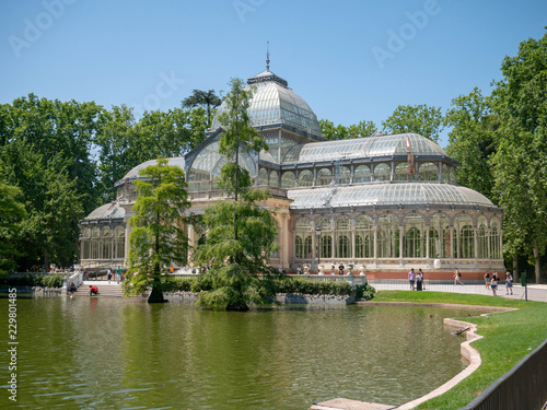 Palacio de Cristal - Glass Palace seen from across a pond in a public park in Parque de Retiro, Madrid, Spain, old historical building in a garden