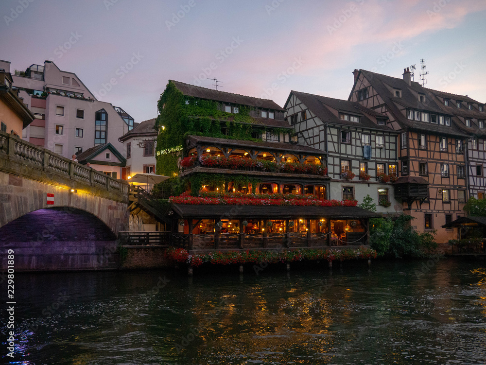 Old classic houses in the traditional fachwerk architectural style reflecting in the water of the canals at night of Strasbourg, France