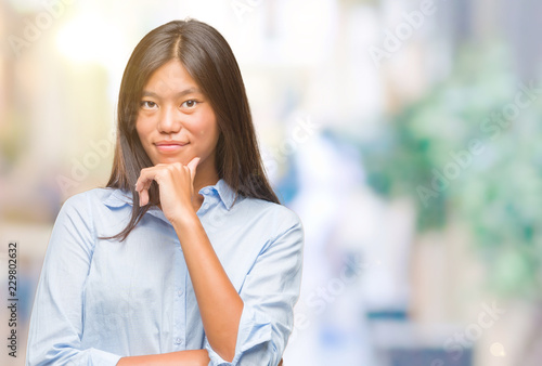 Young asian business woman over isolated background looking confident at the camera with smile with crossed arms and hand raised on chin. Thinking positive.