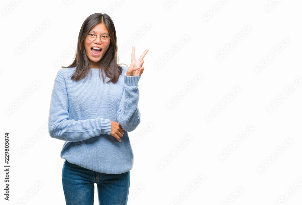 Young asian woman wearing winter sweater over isolated background smiling with happy face winking at the camera doing victory sign. Number two. Young asian woman wearing winter sweater over isolated background smiling with happy face winking at the camera doing victory sign. Number two.