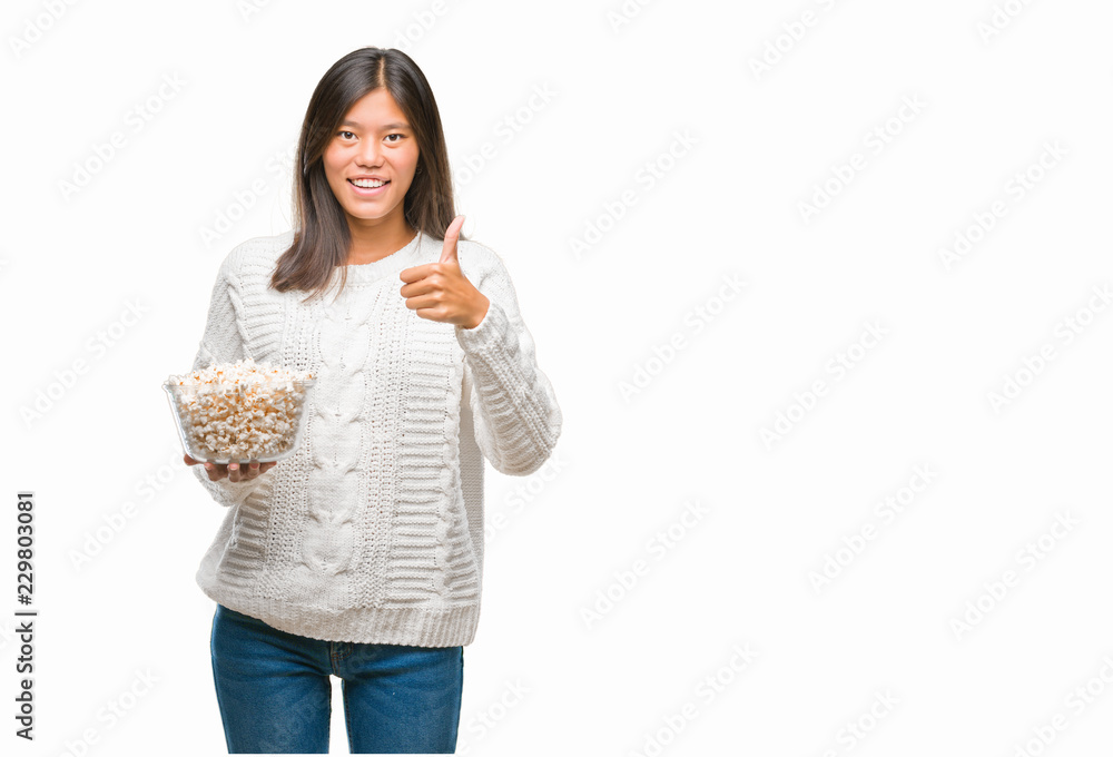 Young asian woman eating popcorn over isolated background happy with big smile doing ok sign, thumb up with fingers, excellent sign Young asian woman eating popcorn over isolated background happy with big smile doing ok sign, thumb up with fingers, excellent sign