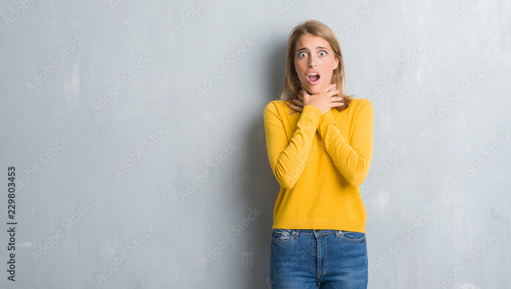 Beautiful young woman standing over grunge grey wall shouting and suffocate because painful strangle. Health problem. Asphyxiate and suicide concept. Beautiful young woman standing over grunge grey wall shouting and suffocate because painful strangle. Health problem. Asphyxiate and suicide concept.