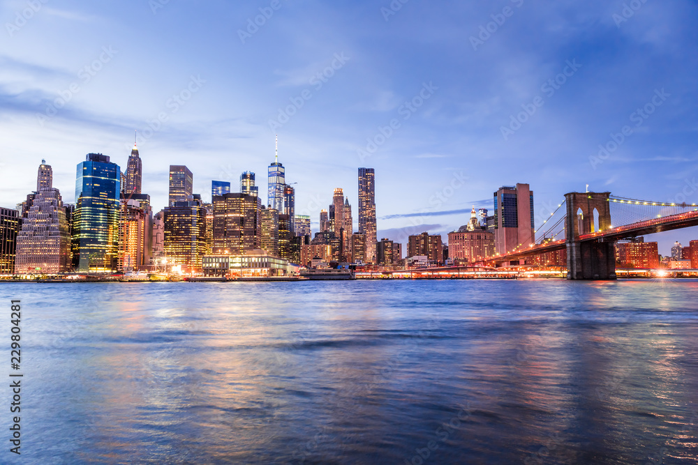 Obraz premium Szeroki kąt widzenia na Nowy Jork Brooklyn Bridge Park w Nowym Jorku nad wschodnią rzeką, panoramę miasta o zmierzchu, zmierzch, niebieska godzina, ciemna noc, drapacze chmur, oświetlone, fala, odbicie, jasne światło