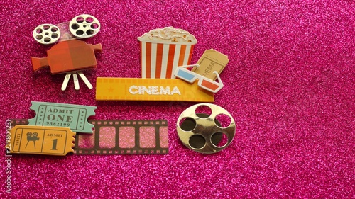 tub of popcorn with cinema sign and 3d glasses movie tickets on film strip movie projector and reel on dark pink shiny background