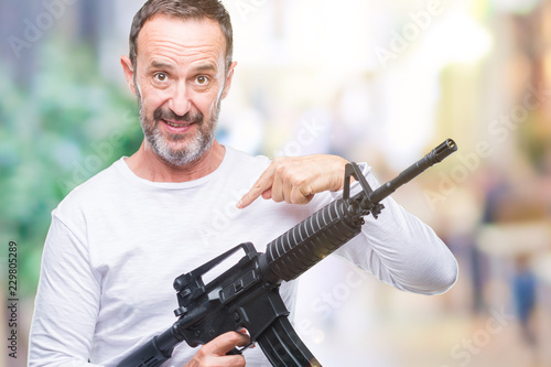 Middle age senior hoary criminal man holding gun weapon over isolated background with surprise face pointing finger to himself