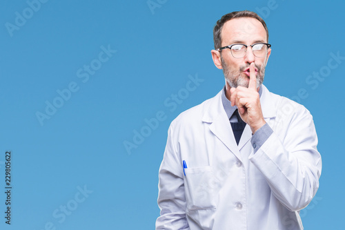 Middle age senior hoary professional man wearing white coat over isolated background asking to be quiet with finger on lips. Silence and secret concept.