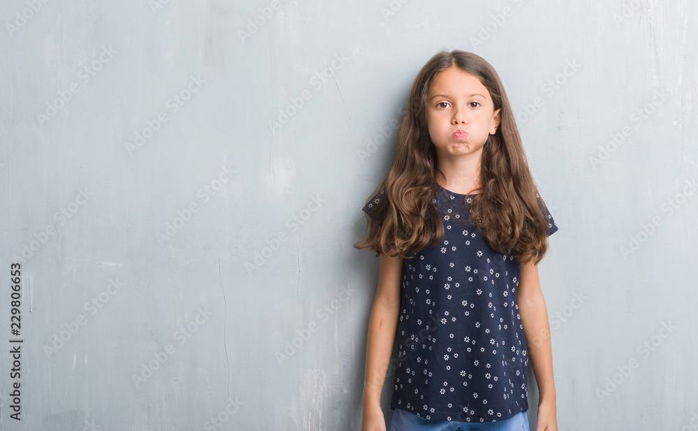 Young hispanic kid over grunge grey wall puffing cheeks with funny face. Mouth inflated with air, crazy expression. Young hispanic kid over grunge grey wall puffing cheeks with funny face. Mouth inflated with air, crazy expression.