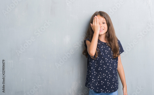 Young hispanic kid over grunge grey wall covering one eye with hand with confident smile on face and surprise emotion. © Krakenimages.com