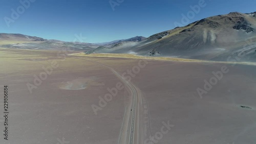 Aerial drone scene of road in desertic landscape with snowy colorful mountains. Rocky golden dry climate . Yellow vegetation in surface. Flying fowards. Catamarca, Argentina photo