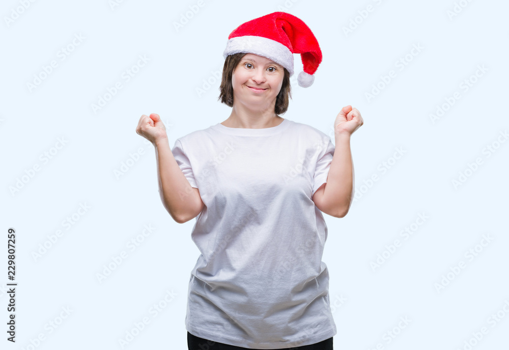Young adult woman with down syndrome wearing christmas hat over isolated background celebrating surprised and amazed for success with arms raised and open eyes. Winner concept. Young adult woman with down syndrome wearing christmas hat over isolated background celebrating surprised and amazed for success with arms raised and open eyes. Winner concept.