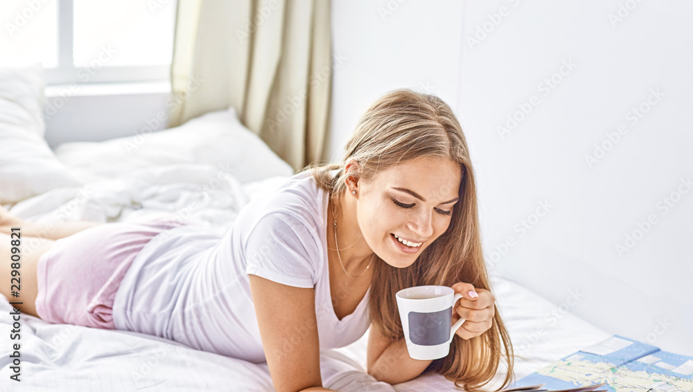 Happy young girl in bed using phone, tablet and maps to search for travel