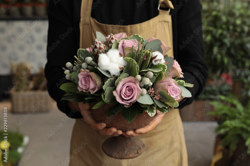 Naklejka premium Festive flower arrangement of paleviolet roses and cotton flowers in the vase florist holding at the flowers boutique.