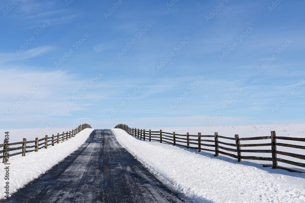 Empty Road and Snow Covered Fields - looking up small hill and bordered by wooden fence