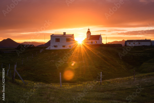 Amazing summer sunset landscape, Iceland. Flowering countryside with small church and sun, travel background