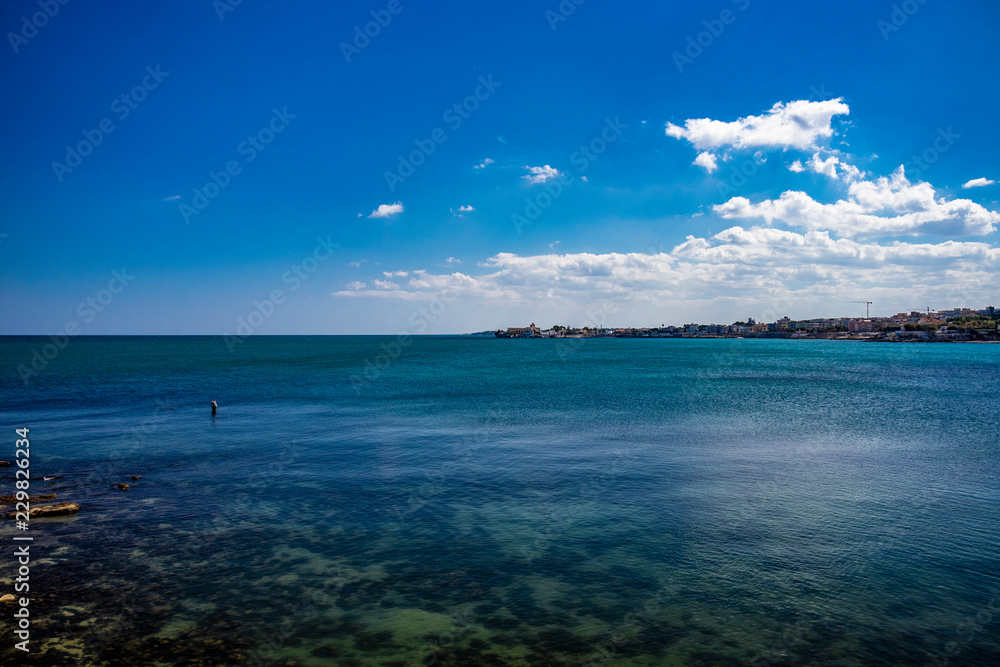 a fisherman fishing in the sea, in the city of Trani, with the Monastery of Santa Maria di Colonna in the background. In Puglia, near Bari, in the province of Barletta, Andria, Trani. Sea and blue sky a fisherman fishing in the sea, in the city of Trani, with the Monastery of Santa Maria di Colonna in the background. In Puglia, near Bari, in the province of Barletta, Andria, Trani. Sea and blue sky