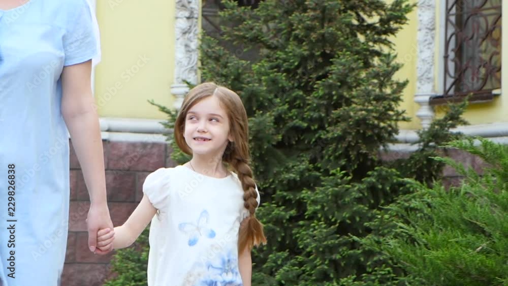 Little girl is holding her mother's hand and walking along the street Little girl is holding her mother's hand and walking along the street