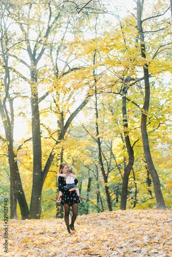 young mother with daughter are walking in the park in the golden autumn