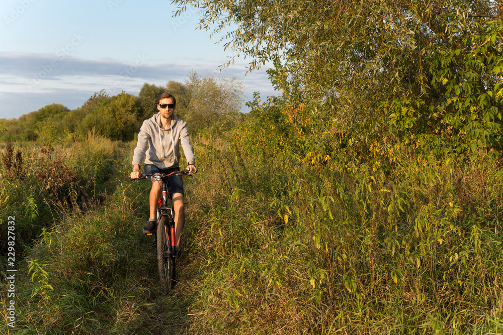 Young man cycling outdoors in summer, autumn landscape in nature