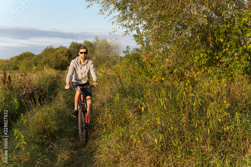 Fototapeta Naklejka Na Ścianę i Meble -  Young man cycling outdoors in summer, autumn landscape in nature