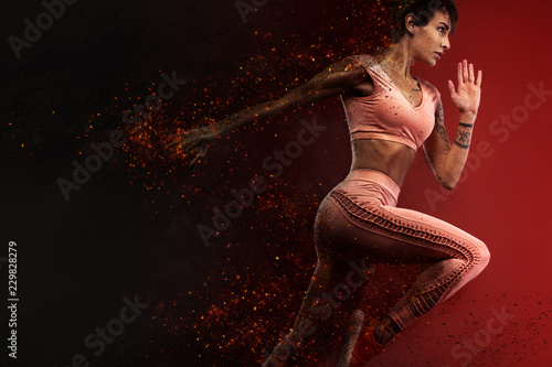 Fitness and sport motivation.. Strong and fit athletic, woman sprinter or runner, running on red background in the fire wearing sportswear. photo