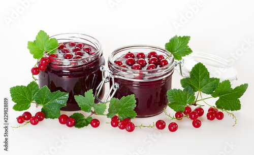 Red currant jam in jars and ripe berries on a white background.
