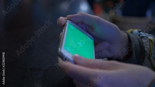 Beautiful girl holding a smartphone in the hands of a green screen green screen, hand of man holding mobile smart phone with chroma key green screen on white background. Gaming smartphone in the cafe.