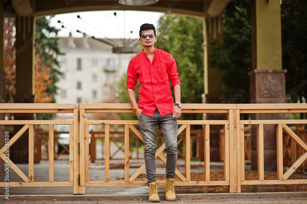Indian man at red shirt and sunglasses posed outdoor.