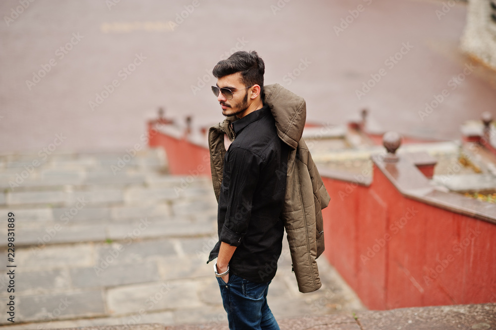 Indian stylish man at black shirt and jacket with sunglasses posed outdoor.