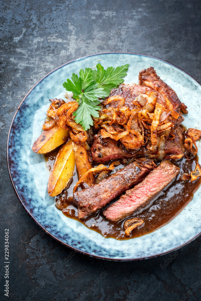 Traditional dry aged sliced roast beef with fried onion rings and potato chips as closeup on a plate with brown sauce Traditional dry aged sliced roast beef with fried onion rings and potato chips as closeup on a plate with brown sauce