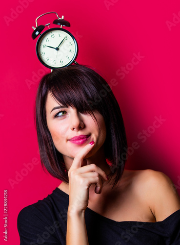 portrait of the beautiful young woman with alarm clock on her head on the vinous background