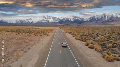 AERIAL: Large SUV drives down empty highway leading to the spectacular Rockies.