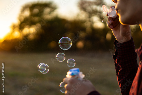 person blow soap bubbles on a sunset in nature field f