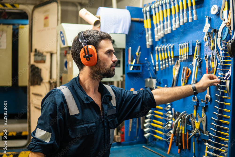 Caucasian marine engineer officer in engine control room ECR. He works in  workshop and chooses correct tools and equipment Stock Photo
