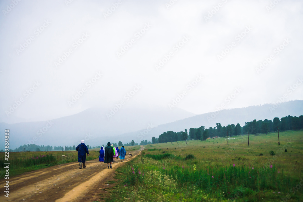 People go forward in mountain despite bad weather. Travelers with dog goes upwards along road. Way on foot in highlands in rainy overcast day. Summit despite everything. Walking in mountains.