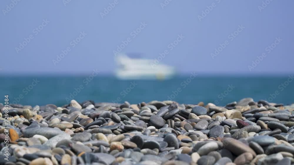 Pebbles on sunny beach with blurry ship at sea panning left to right Pebbles on sunny beach with blurry ship at sea panning left to right