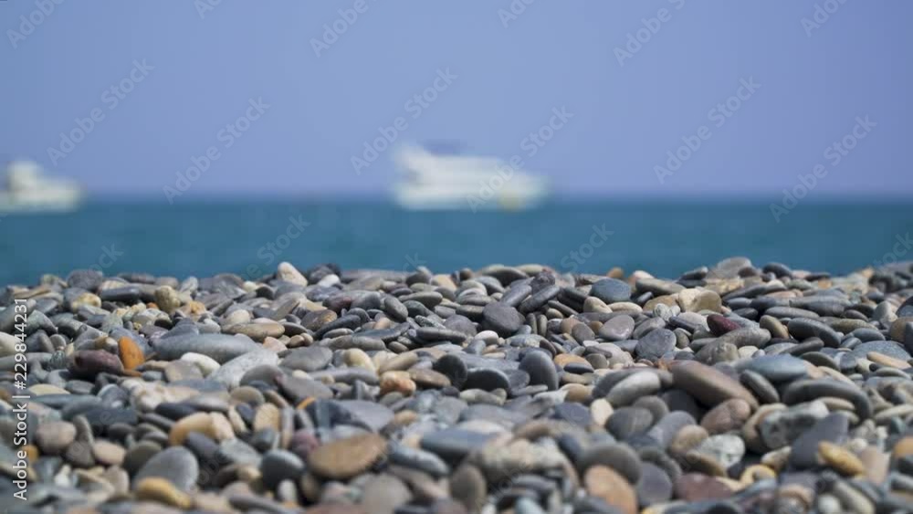 Pebbles on sunny peaceful beach with blurry ship at sea wide angle Pebbles on sunny peaceful beach with blurry ship at sea wide angle