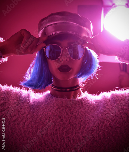 Woman in fashion winter concept wearing gold hat cap round sunglasses in pink neon light 