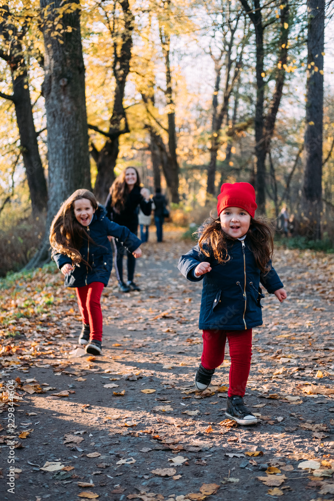 children running and playing in autumn park. two beautiful caucasian girls wearing cute trendy outfit having fun outdoors children running and playing in autumn park. two beautiful caucasian girls wearing cute trendy outfit having fun outdoors