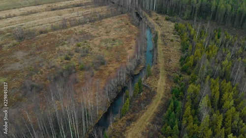 Aerial, tilt in, drone shot, towards a river, surrounded by leafless, autumn forest and fields, on a cold, cloudy, fall day, in Juuka, North Karelia, Finland photo