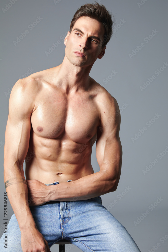 A handsome muscular, shredded man without a shirt, sitting on a chair in  the studio wears only blue jeans. His fitness oiled body is shining. Stock  Photo | Adobe Stock