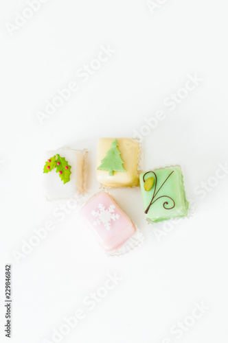 White, light pink, yellow and green petit fours, small cake squares decorated with fondant, chocolate, sugar icing and marzipan Christmas ornaments