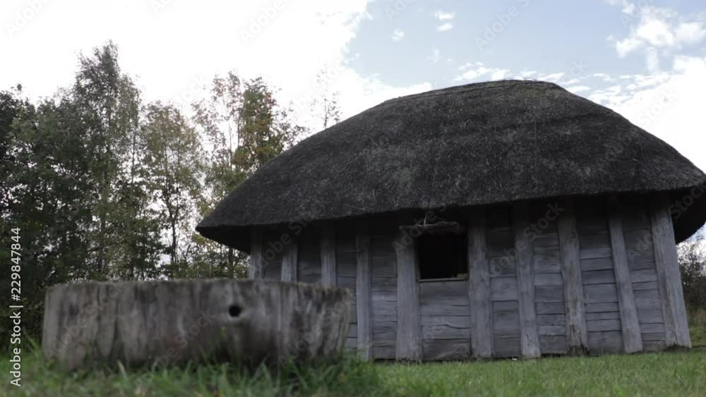 Small medieval hut in the country side. Tree stump in the foreground with a blue sky in the background. Group of trees to the right. Small medieval hut in the country side. Tree stump in the foreground with a blue sky in the background. Group of trees to the right.