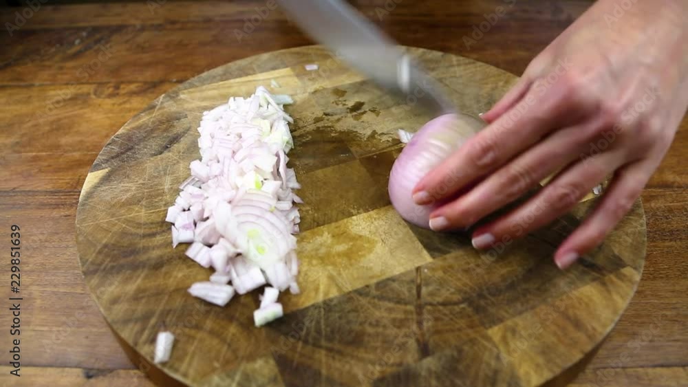 Onion is finely chopped on a wooden board using a large stainless steel chef's knife. Onion is finely chopped on a wooden board using a large stainless steel chef's knife.