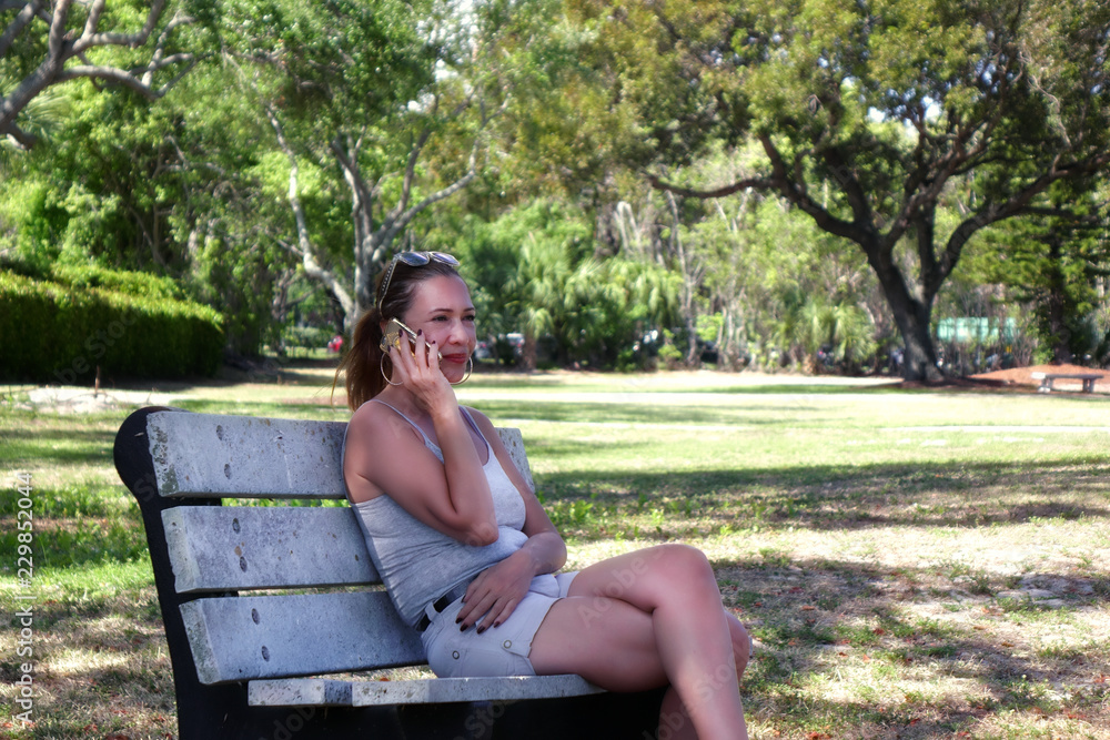 Outdoor portrait of a young adult woman sitting on park bench using cell phone in Florida, USA Outdoor portrait of a young adult woman sitting on park bench using cell phone in Florida, USA