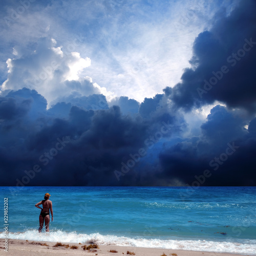 Young adult woman in bikini relaxing on sandy beach over cloudy storm sky