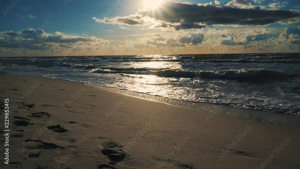 sunset behind clouds over sea waves and sandy beach in summer sunset behind clouds over sea waves and sandy beach in summer