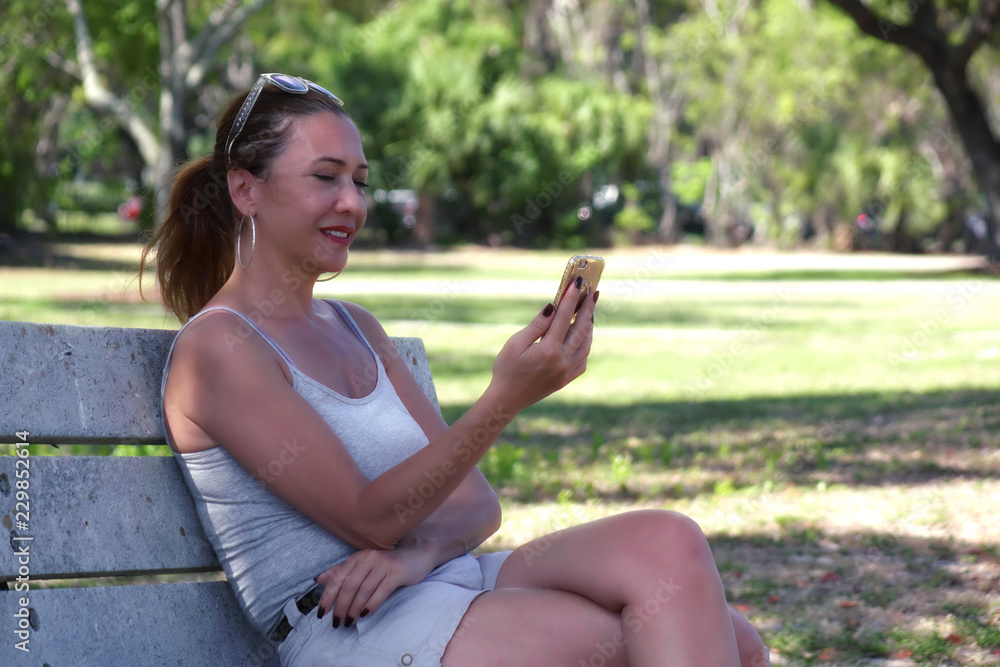 Outdoor portrait of a young adult woman sitting on park bench using cell phone in Florida, USA Outdoor portrait of a young adult woman sitting on park bench using cell phone in Florida, USA