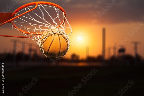 Basketball ball falling into net on sunset background